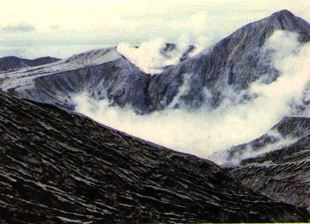 Ash mantles the summit of Colo volcano after a powerful explosive eruption in 1983.  The volcano forms the isolated island of Una-Una in the middle of the Gulf of Tomini in northern Sulawesi.  The broad, low volcano is truncated by a 2-km-wide caldera that contains a small central cone.  Only three eruptions have been recorded in historical time.  The last eruption, in 1983, produced pyroclastic flows that swept over most of the island shortly after all residents had been evacuated.     Photo by M.S. Santoso, 1983 (Volcanological Survey of Indonesia).