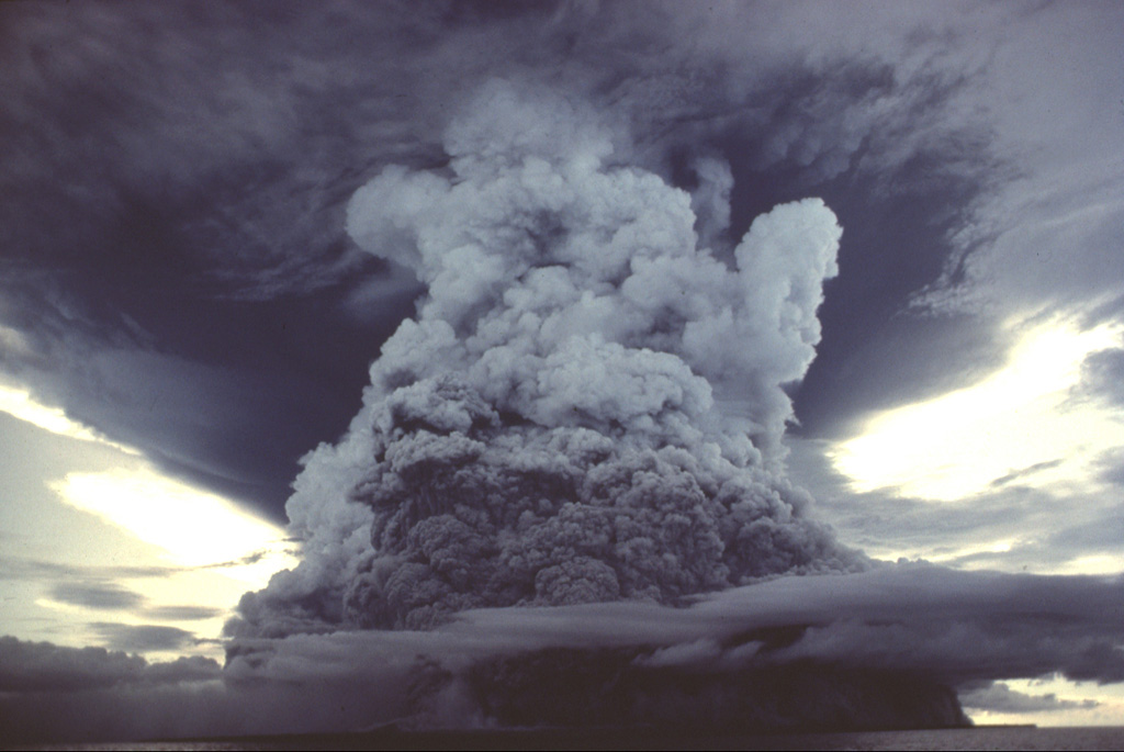 A powerful eruption column rising above Colo volcano is seen from the south on August 22, 1983.  Pyroclastic flows from this explosion continued 500 m beyond the SSW coast of the island and 1 km beyond the NNW coast.  This photo was taken about one month after the paroxysmal eruption on July 23, which produced pyroclastic flows that swept over virtually the entire island. Copyrighted photo by Katia and Maurice Krafft, 1983 (published in SEAN Bulletin v 8, 1983).
