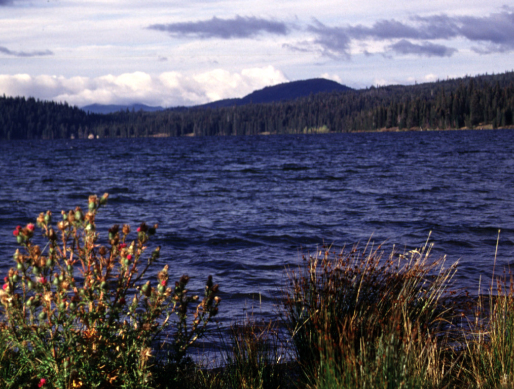 Cinnamon Butte (right center) rises above the shore of Diamond Lake, around 30 km N of Crater Lake. The cone is relatively young, having formed around 7,780 and 15,000 years ago. Lava flows from Cinnamon Butte traveled north and covered around 28 km2. Photo by Lee Siebert, 1997 (Smithsonian Institution).