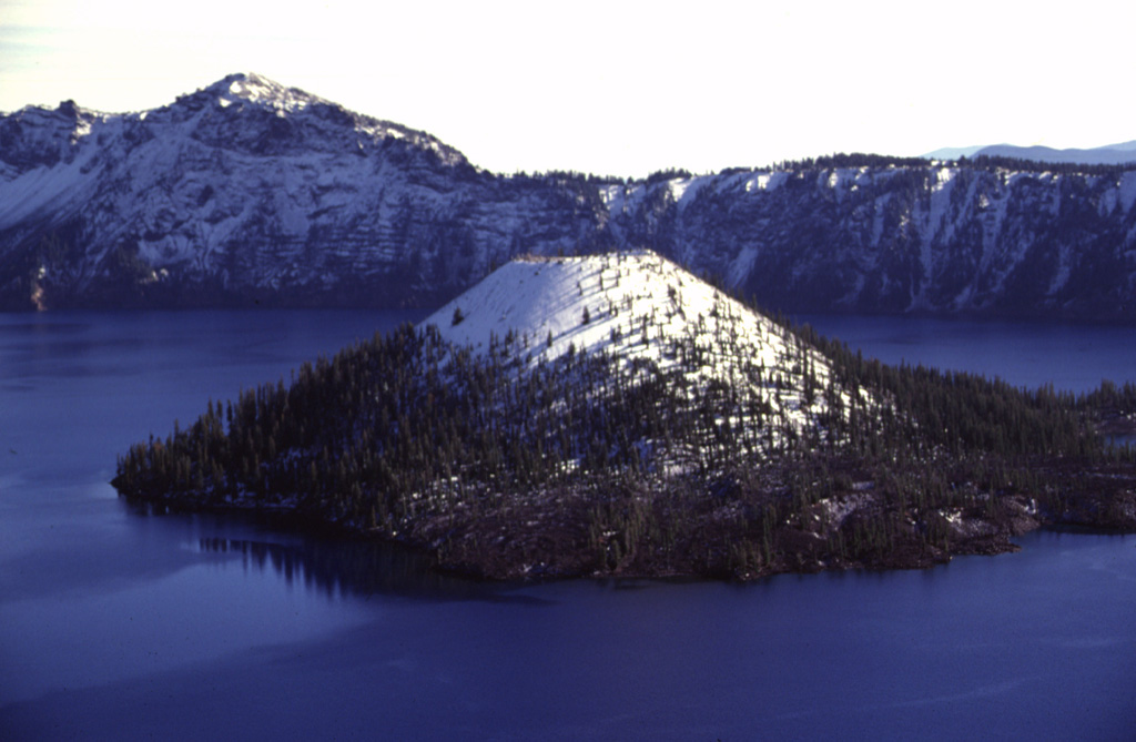 Wizard Island is the only one of three post-caldera cones within the Crater Lake caldera. The symmetrical scoria cone has a 90-m-wide summit crater. It formed several hundred years after the collapse of Mount Mazama about 7,700 years ago along the western structural margin of the caldera. Much of the cone lies beneath the nearly-600-m-deep waters of Crater Lake. A small dome is located on a central platform below the water and east of Wizard Island. Photo by Lee Siebert, 1997 (Smithsonian Institution).