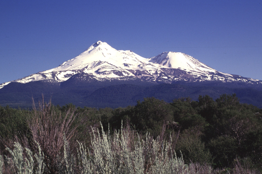 Massive Mount Shasta, the largest-volume volcano of the Cascade Range in northern California. It is seen here from the north, with Hotlum cone forming the summit and Shastina on the western flank. It is composed of at least four main edifices, of which the last two, Hotlum and Shastina, are of Holocene age. Photo by Lee Siebert, 1998 (Smithsonian Institution).