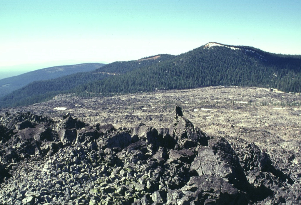The Glass Mountain obsidian flow buries much of the eastern rim of Medicine Lake caldera.  The massive 1 cu km flow traveled south towards Lyons Peak (upper right) before the bulk of the flow was diverted to the east and descended the caldera's outer flank.  The latest event at Glass Mountain produced the craggy rhyolitic obsidian dome seen in the foreground.  The roughly 900-year-old flow is the youngest and largest of a series of Holocene rhyolitic and dacitic lava flows at Medicine Lake. Photo by Lee Siebert, 1998 (Smithsonian Institution).