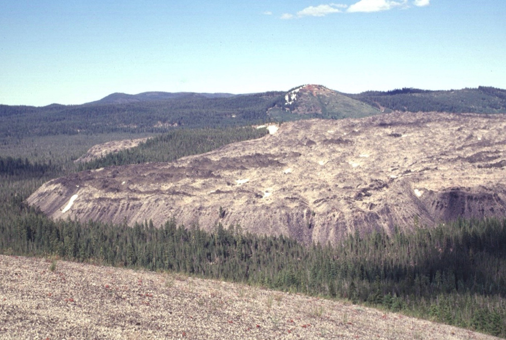The Little Glass Mountain obsidian flow is seen here from Pumice Stone Mountain, named for the mantle of white pumice (foreground) from Little Glass Mountain. The 0.4 km3 obsidian flow was erupted from a currently buried vent below the Little Mt. Hoffman cone seen here behind the flow. The Little Glass Mountain pumice eruption and obsidian flow occurred about 950 years ago during one of the more recent eruptions from Medicine Lake. Photo by Lee Siebert, 1998 (Smithsonian Institution).