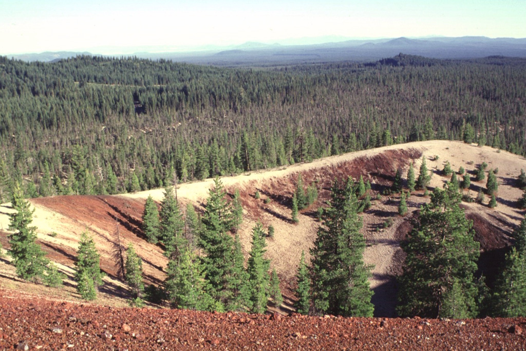 Paint Pot Crater on the lower SW flank of Medicine Lake volcano derives its name from the mantle of white pumice from nearby Little Glass Mountain that covers the reddish oxidized scoria of the cinder cone.  Paint Pot Crater emitted a lava flow from its breached crater that traveled to the south, where it forms the sparsely vegetated area seen in the photo beyond the far rim of the cone.  The crater and lava flow are among the youngest products of Medicine Lake volcano, and were erupted about 1100-1150 years ago.  Photo by Lee Siebert, 1998 (Smithsonian Institution).