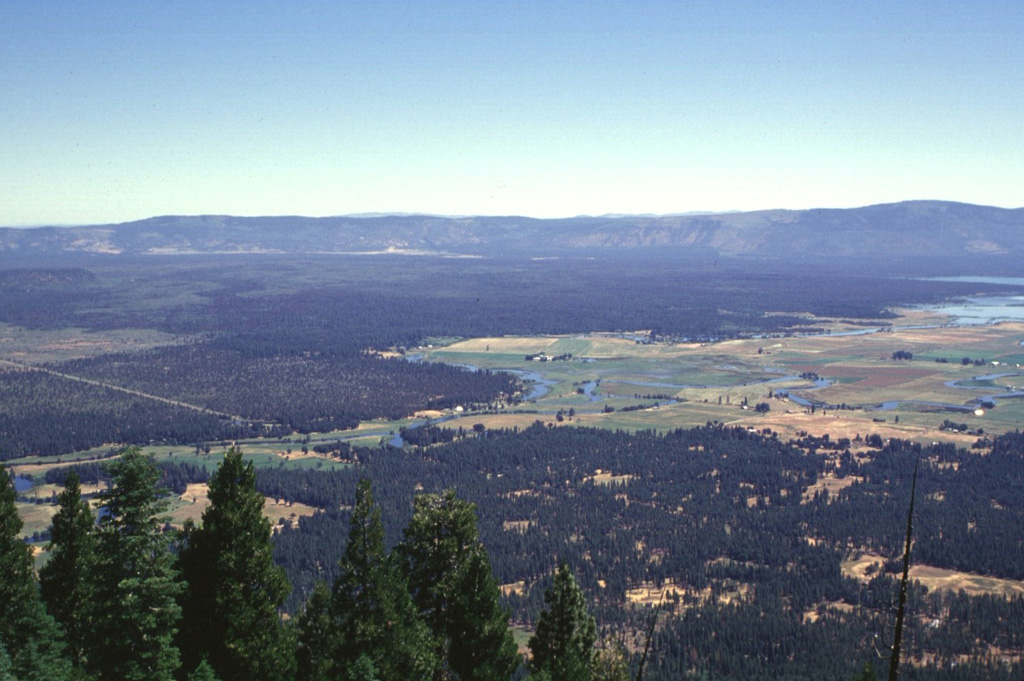 The broad forested area in the center of the photo, below the Big Valley Mountain fault scarp on the horizon, is a series of youthful lava flows erupted from Brushy Butte, a small low shield volcano barely distinguishable in this photo.  Big Lake, at the extreme right, was formed by numerous springs issuing from the margin of the basaltic lava flows.  This view from the SW is from the summit of Soldier Mountain. Photo by Lee Siebert, 1998 (Smithsonian Institution).