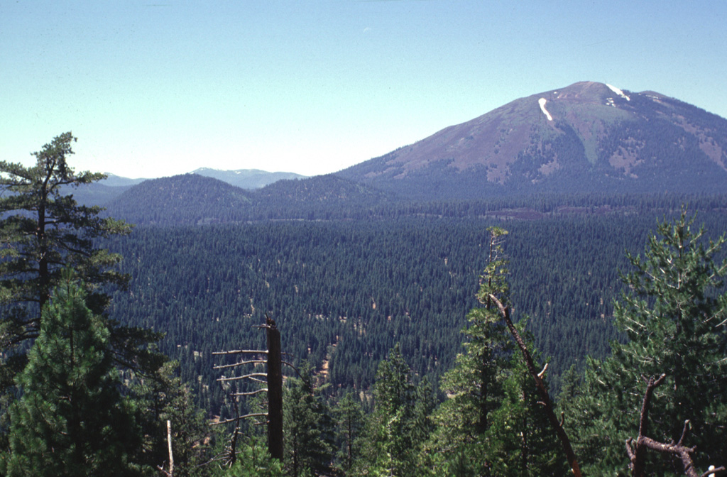 Twin Buttes, the two cinder cones at left-center, were formed SE of Burney Mountain, the prominent andesitic lava dome complex at the right.  Blocky, partially vegetated lava flows extend to the north from the cinder cones.  The twin cones are part of a large area of young volcanism located north of Lassen National Park.  Burney Mountain is a large dacitic complex of five overlapping lava domes of Pleistocene age. Photo by Lee Siebert, 1998 (Smithsonian Institution).