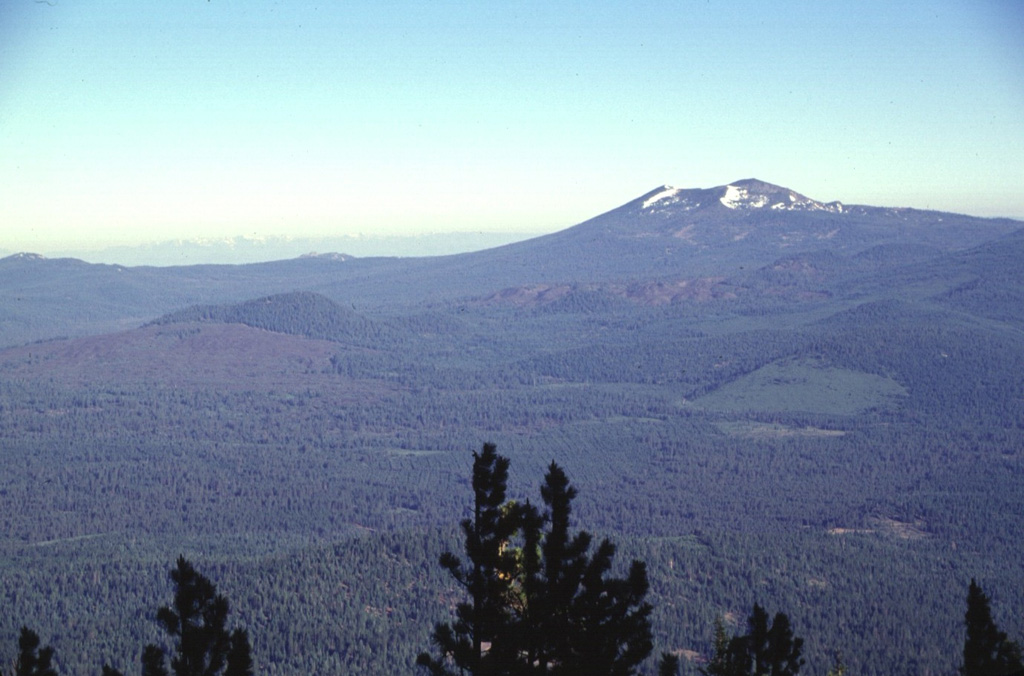 A N-S-trending chain of vents extending across the center of the photo forms Tumble Buttes, a young volcanic field north of Lassen Volcanic National Park.  A large area of unvegetated lava flows at the left margin originated from Bear Wallow Butte at the southern end of the chain.  Other young unvegetated flows form the Devils Rock Garden at right-center, below Crater Mountain, the prominent snow-dappled peak on the horizon.  This view looks to the NW across the Hat Creek valley from West Prospect Mountain. Photo by Lee Siebert, 1998 (Smithsonian Institution).