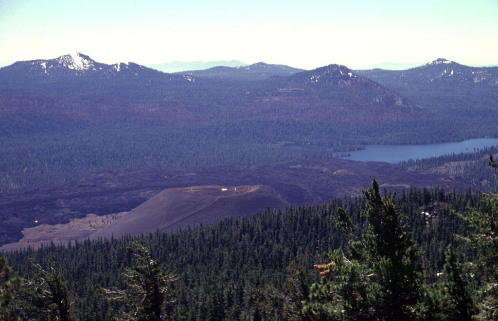 The unvegetated pyroclastic cone in the foreground, seen from near the summit of Prospect Peak, is Cinder Cone in NE Lassen Volcanic National Park.  Cinder Cone, which was formed during an eruption several hundred years ago, was the source of an extensive series of lava flows that can be seen on the far side of the cone.  The flows dammed up local drainages, forming two lakes, one of which is Snag Lake, seen here SSE of the cone. Photo by Lee Siebert, 1998 (Smithsonian Institution).