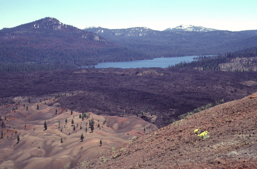 A series of lava flows from a vent on the SE flank of Cinder Cone traveled about 3.5 km to the north and south.  Snag Lake, seen here to the south from the summit of Cinder Cone, was formed with the lava flow dammed up drainages.  The colorful area at the lower left, known as the Painted Dunes, is an ash deposit oxidized by the heat of a still-hot underlying lava flow.  The dark-colored main flow beyond the Painted Dunes was emplaced later during the same eruption, and is ash free. Photo by Lee Siebert, 1998 (Smithsonian Institution).