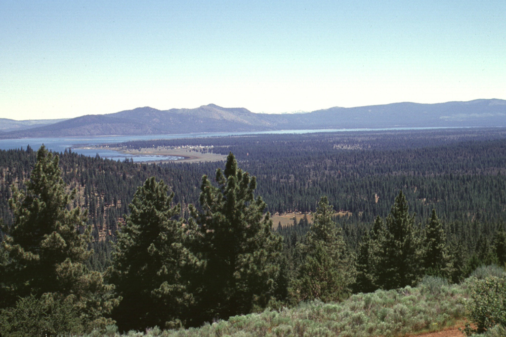 Forest-covered Brockman Flat, formed by lava flows from a chain of cinder cones in the Eagle Lake volcanic field, extends into Eagle Lake.  The cinder cones, out of view to the right, were formed along N-S-trending faults within the Eagle Lake volcano-tectonic depression, whose SE margin forms the peaks beyond Eagle Lake.  The flows from the depression represent the southernmost late-Quaternary magmatism associated with backarc spreading in the NW Great Basin. Photo by Lee Siebert, 1998 (Smithsonian Institution).