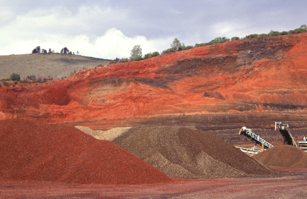 Brilliantly colored, bright-red oxidized scoria deposits from a cinder cone near the SE end of Clear Lake are quarried for road aggregate.  The basaltic-andesite cinder cone is one of a N-S-trending chain of young cones at the eastern margin of the Clear Lake volcanic field.  This the northernmost of two quarried cinder cones bissected by the highway leading into the town of Clearlake Oaks. Photo by Paul Kimberly, 1997 (Smithsonian Institution).