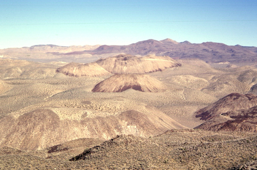 The Coso volcanic field at the western edge of the Basin and Range province consists of largely Pliocene to late-Pleistocene rhyolitic lava domes and basaltic cinder cones covering a 400 sq km area.  This view looks south across the range from Cactus Peak with some of the 38 light-colored rhyolitic lava domes of the Coso volcanic field in the foreground and dark-colored basaltic cinder cones and associated lava flows in the background.  Active fumaroles and thermal springs are present in an area that is a producing geothermal field.  Photo by Paul Kimberly, 1997 (Smithsonian Institution).