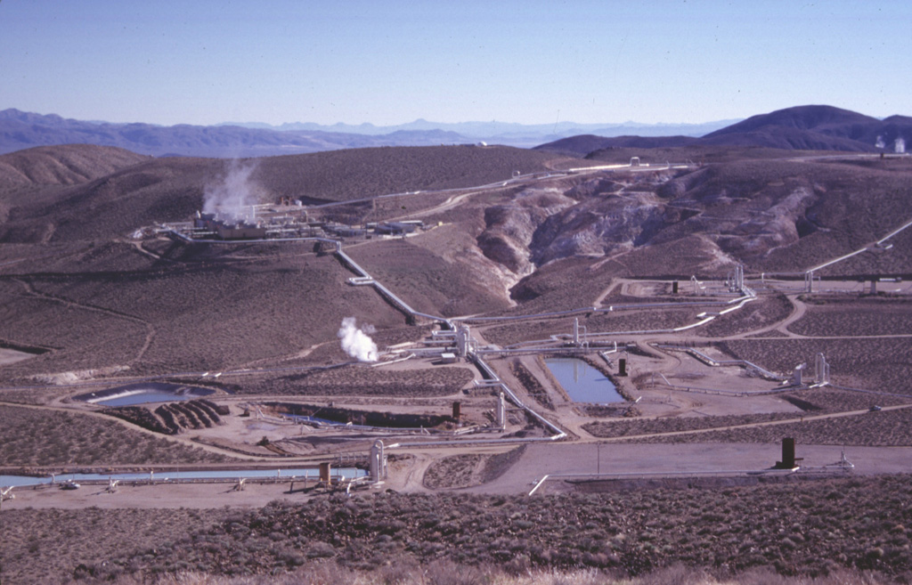 A cooperative program of the U.S. Navy China Lake Naval Weapons Station and private industry has developed geothermal power at the Coso volcanic field.  The first well was drilled in 1981 and production now exceeds 250 megawatts, greatly reducing energy costs to the Navy and providing additional electricity to the southern California power grid.  This view from the NW shows turbine plants and production well ponds at Coso.  Devils Kitchen, a fumarolic area with extensively hydrothermally altered ground, appears at the upper right. Photo by Paul Kimberly, 1997 (Smithsonian Institution).