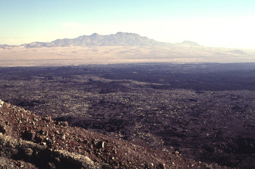 The NE rim of Pisgah Crater provides a view of the 100-sq-km lava field surrounding the crater.  The basaltic lava field was erupted from the crater and nearby vents and is dominantly formed of pahoehoe lava, although aa lavas were erupted on the eastern side.  Interstate highway 40 skirts the northern margins of the lava flow, below the Cady Mountains in the distance.  The lavas were erupted onto alluvial-fan and playa-lake deposits.   Photo by Lee Siebert, 1997 (Smithsonian Institution).