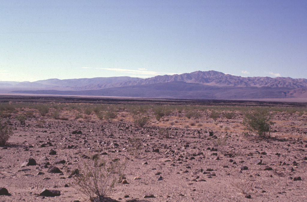 The dark-colored area seen in the distance across the dry Lavic Lake is a cinder cone and associated lava field that is one of the young vents of the Lavic Lake volcanic field.  The youthful-looking lava flows originated from the Sunshine Peak area of the Lava Beds Mountains, south of the better known Pisgah Crater. Photo by Paul Kimberly, 1997 (Smithsonian Institution).