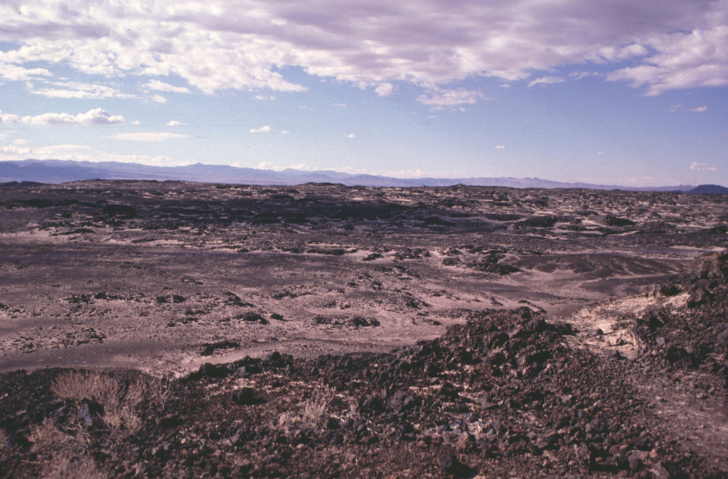 The 70-sq-km Amboy lava field in southern California is composed mostly of vesicular pahoehoe lava flows that form a hummocky terrain with a surface relief of 2-5 m.  Lava tubes are not present in the Amboy flows, which display abundant tumuli and pressure ridges.  Light-colored deposits of aeolian sand, thicker to thw SW, fill depressions in the lava flow.    Photo by Paul Kimberly, 1997 (Smithsonian Institution).