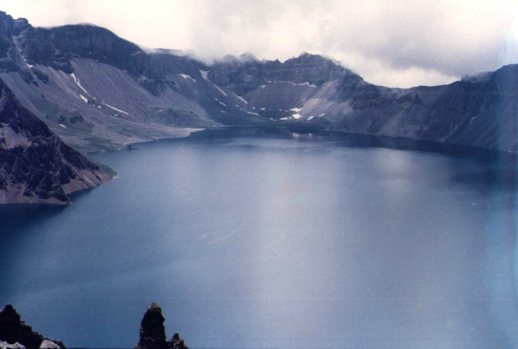 Lake Tianchi occupies the 5-km-wide, 850-m-deep summit caldera of Changbaishan, which straddles the China/Korea border. The volcano is also known as Baitoushan and by the Korean names of Baegdu or P'aektu-san. This view looks from the northern rim on the Chinese side towards the SE caldera wall on the Korean side. One of the world's largest known Holocene explosive eruptions took place from Changbaishan about 1000 CE, depositing tephra as far away as northern Japan. Photo by Xiang Liu, 1983 (Changchun University).