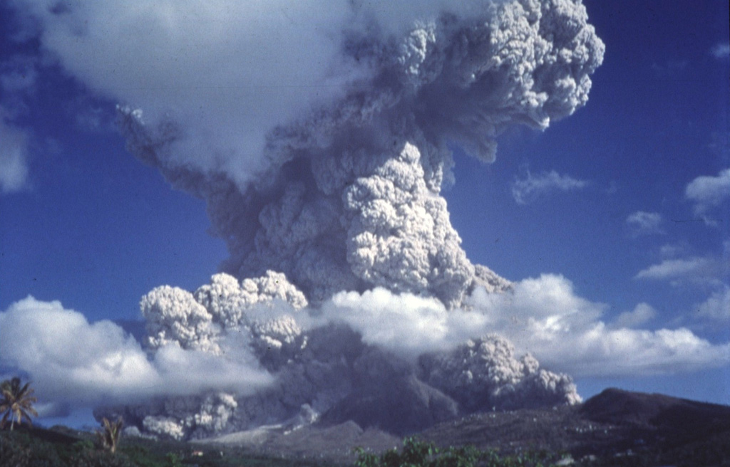 A towering ash cloud rises above the summit of Soufrière Hills volcano on October 20, 1997, as pyroclastic flows sweep down the flanks of the volcano.  This photo was taken from the old volcano observatory 7 km NW of the volcano two minutes after the start of the explosion. Photo by Paul Cole, 1997 (Montserrat Volcano Observatory).