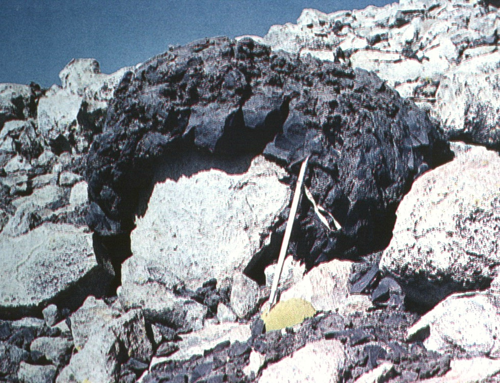 A dark-colored andesitic volcanic bomb, ejected in a plastic state with a ballistic trajectory, drapes older rhyolitic rocks.  The bomb was ejected during the Ajata volcanic eruptions. Helium surface-exposure ages ranging between about 1385 and 6500 years ago were obtained from the three lava flows erupted from the Volcanes de Ajata.  Note the ice axe for scale (right-center). Photo by Oscar González-Ferrán (University of Chile).