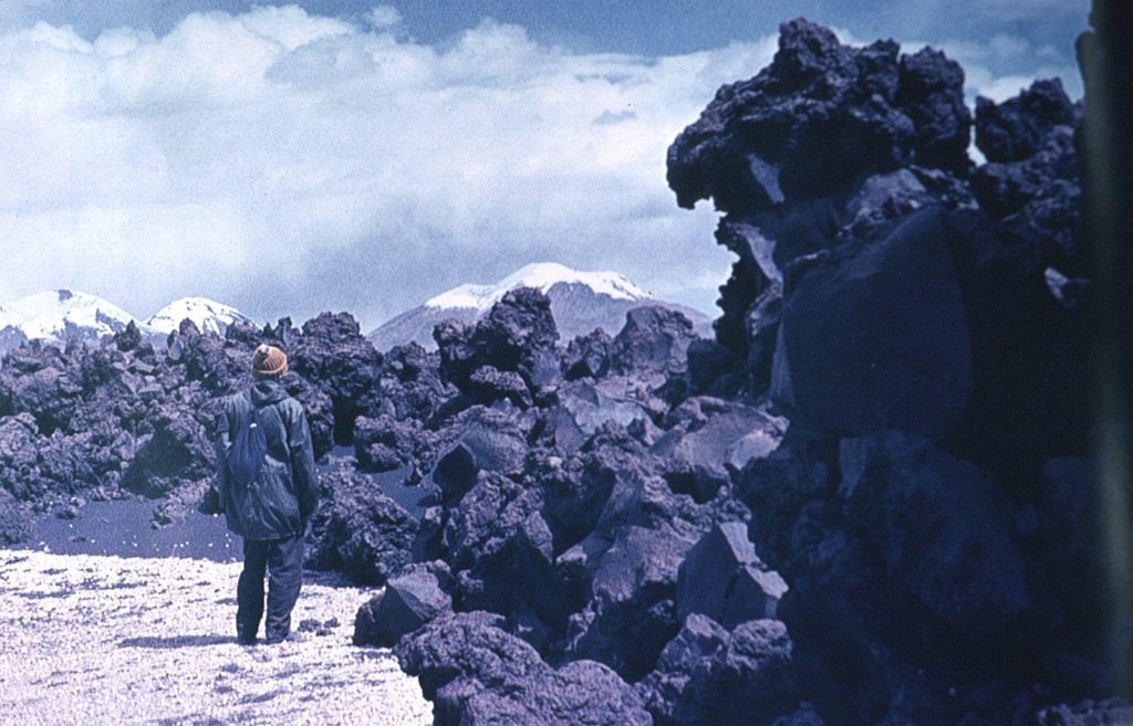 This viscous andesitic aa flow was erupted from the Volcanes de Ajata cinder cones along a N-S fracture on the southern flank of Parinacota.  Helium-exposure ages of about 5985 and 6500 years ago were obtained from the lowermost and oldest of three lava flows of the Volcanes de Ajata.  Snow-capped Acotango, Sajama, and Guallatiri volcanoes form the horizon to the east. Photo by Oscar González-Ferrán (University of Chile).