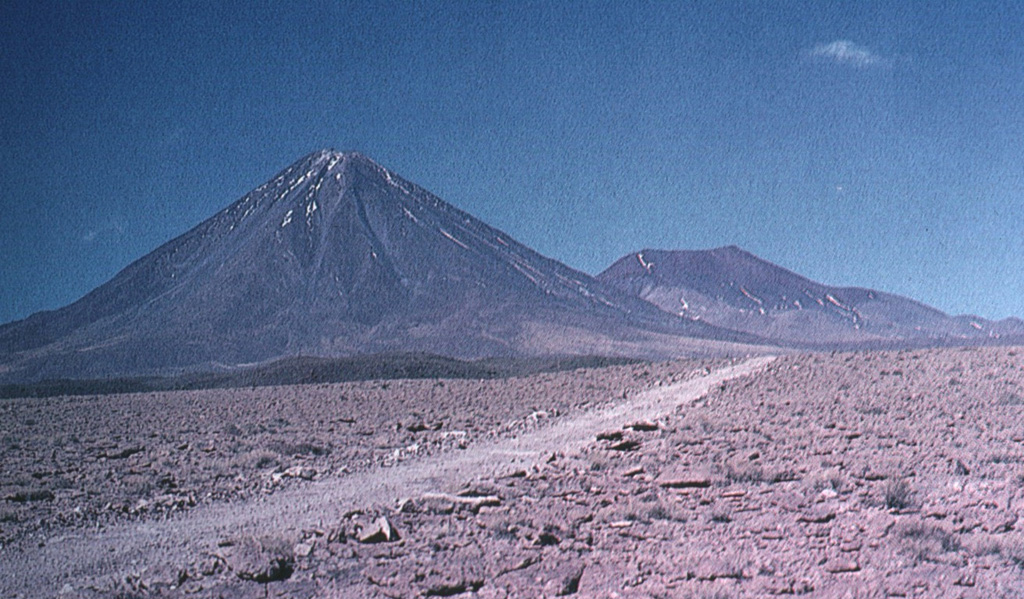 The symmetrical Licancabur stratovolcano (left) rises above a basement of rhyodacitic ignimbrites and dacitic lava domes.   A small 80-m-wide lake, one of the world's highest, occupies its 400-m-wide summit crater.  Archaeological ruins were found on the 5916-m-high crater rim of Volcán Lincancabur.  Young lava flows with prominent levees extend up to 6 km down the NW-to-SW flanks of the volcano. Photo by Oscar González-Ferrán (University of Chile).