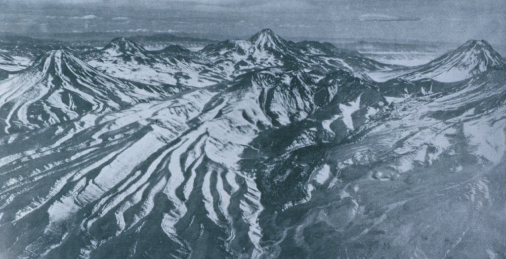 Colachi (left) is an andesitic-dacitic stratovolcano whose most recent activity produced pristine silicic lava flows of probable Holocene age.  The largest of these covers a 7 km2 area on the saddle between Colachi and the neighboring volcano of Acamarachi (center horizon).  This aerial view from the west also shows the conical peak of Aguas Calientes (far right), a twin volcano of Lascar volcano, whose slopes appear at the lower right.  The Talabre valley in the center foreground is partially filled by an andesitic lava flow from Lascar. Photo by Insitituto Geográfico Militar, courtesy of Oscar González-Ferrán (University of Chile).