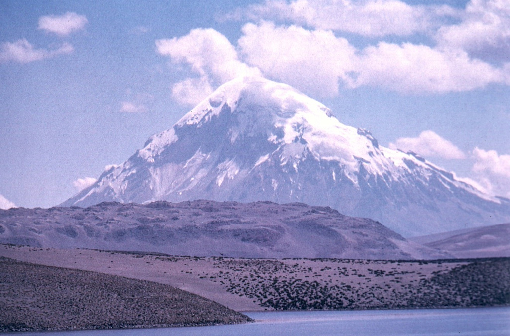 Sajama volcano in Bolivia towers beyond the Chilean border above Laguna Chungará.  Blocky Pleistocene lava flows from Parinacota volcano, out of view to the left, extend across the middle of the photo.  Sajama is Bolivia's highest peak and rises about 2000 m above its base.  The dominantly andesitic volcano overlies andesitic-to-rhyolitic lava domes. Photo by Oscar González-Ferrán (University of Chile).