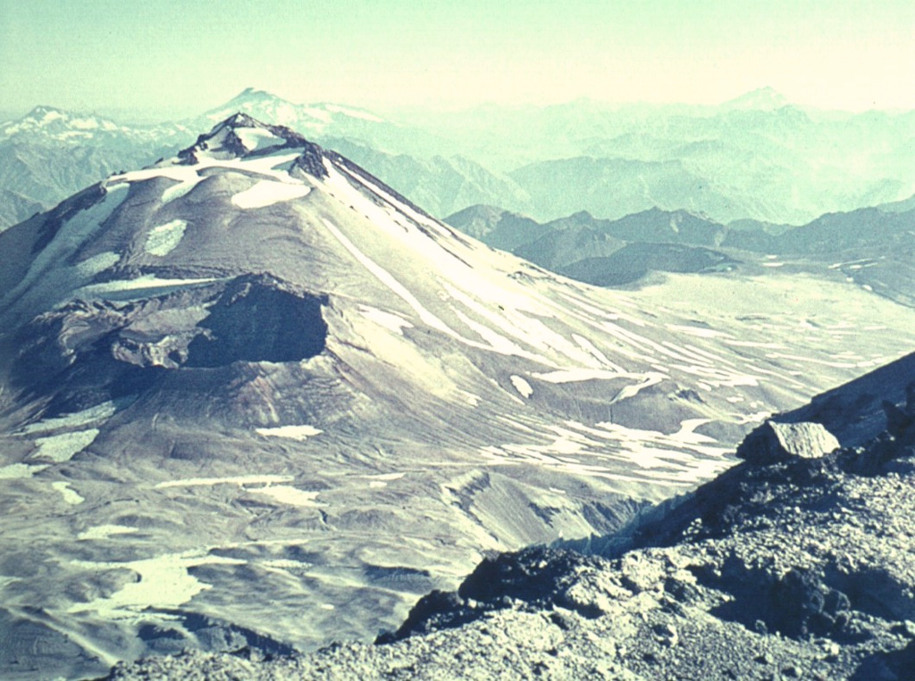 The gaping crater of the 1932 Quizapú eruption (left-center) lies below the summit of Cerro Azul stratovolcano.  Cerro Azul was constructed to the south of its twin volcano Descabezado Grande, where this photo was taken.  Steep-sided Cerro Azul has a 500-m-wide summit crater that is open to the north. Quizapú was the source of one of the world's largest explosive eruptions of the 20th century in 1932.  This eruption created a 600-700 m wide, 150 m deep crater and ejected 9.5 cu km of dacitic tephra. Photo by Oscar González-Ferrán (University of Chile).