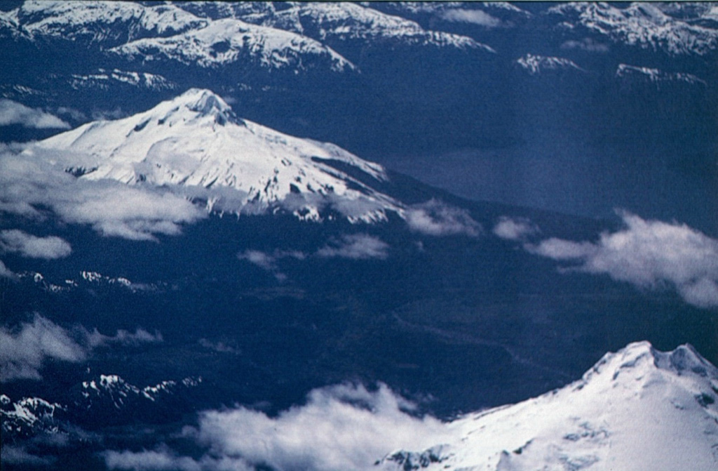 Volcán Cay (upper left), is located east of Macá volcano (lower right) and NW of the town of Puerto Aisén.  The basaltic and dacitic stratovolcano has an explosion crater that is open to the east, and about a half dozen explosion craters and pyroclastic cones lie along a fissure trending SW of the summit.  Another 10 basaltic pyroclastic cones are located along second parallel fissure 5 km to the SE that is part of the major regional Liquiñe-Ofqui fault zone.   Photo by Oscar González-Ferrán (University of Chile).