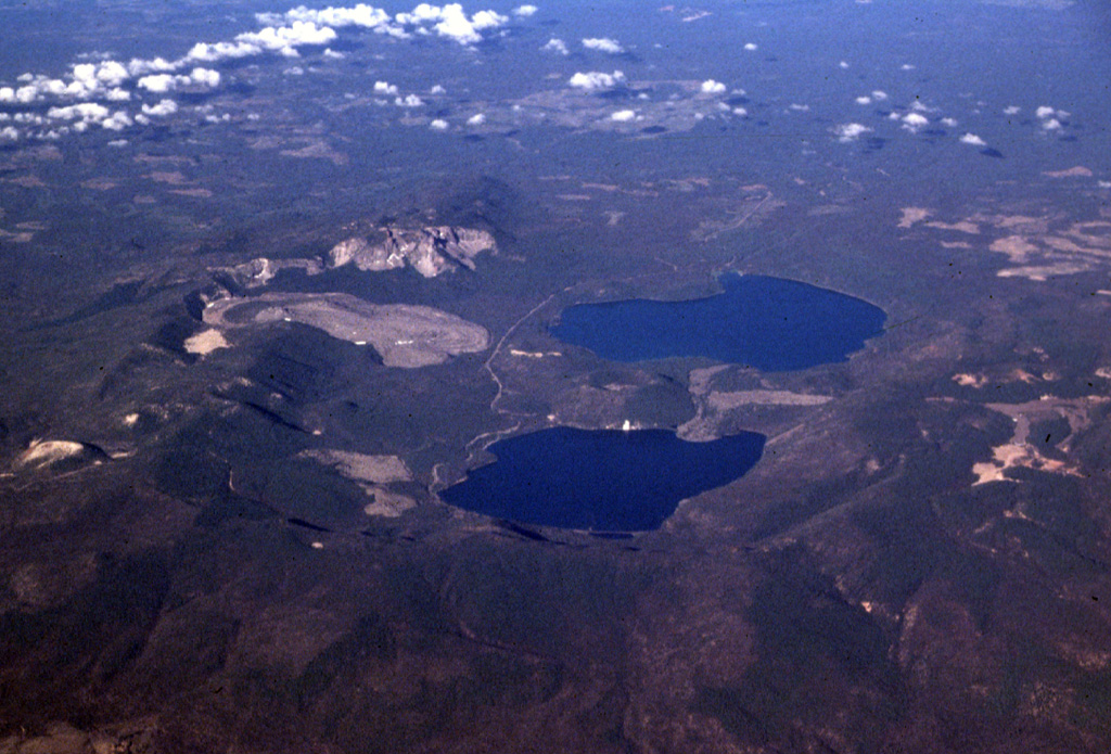 Newberry caldera is one of the largest volcanoes in the conterminous United States, covering an area of about 3,200 km2. Two lakes, Paulina Lake (top) and East Lake (bottom) partially fill the 6.5 x 8 km wide caldera, which formed following the eruption of major pyroclastic flows during the Pleistocene. Subsequent eruptions have taken place from vents within the caldera, near its rim, and from fissures on its flanks. The light-colored lobate lava flow south (left) of Paulina Lake is one of several obsidian flows erupted during the Holocene. Photo by Lee Siebert, 1998 (Smithsonian Institution).