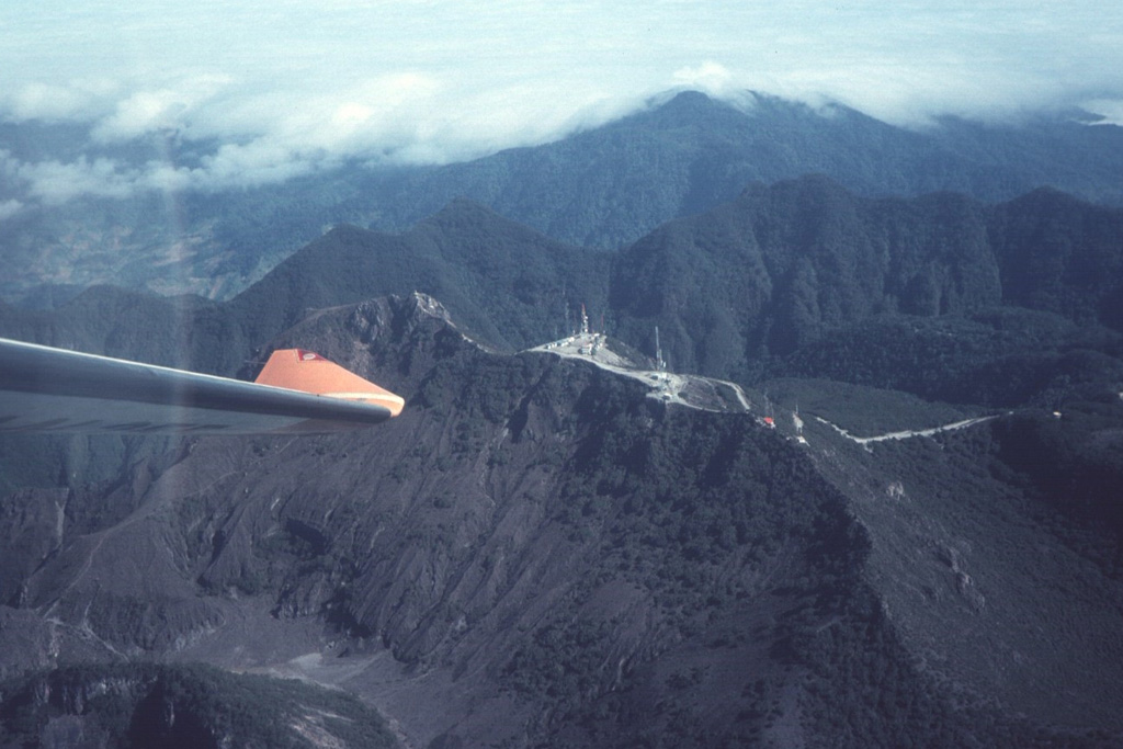 The summit of Barú volcano is just above the wing tip in this view from the SE. Communication towers line the ridge to the right of the summit. Behind it is the northern wall of a large horseshoe-shaped collapse scarp. The Pleistocene Volcán Colorado is under clouds to the upper right. Photo by Tom Casadevall, 1994 (U.S. Geological Survey).