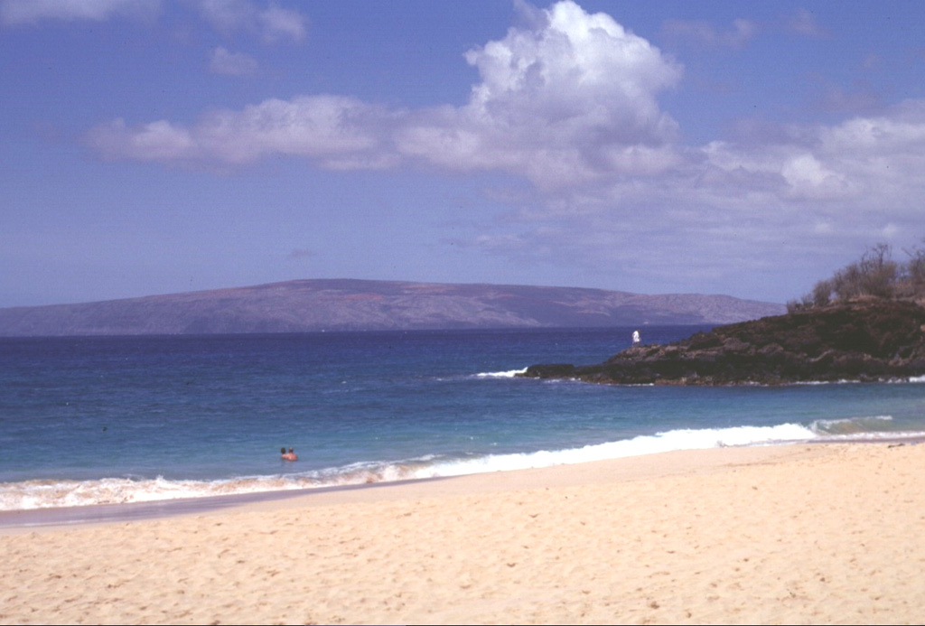 The uninhabited island of Kahoolawe is seen here rising to the SW across a narrow channel from Oneloa beach on the island of Maui.  Kahoolawe consists of a broad, low shield volcano formed by Pleistocene eruptions along a rift zone that extends SW from a buried, 5-km-wide caldera at the eastern side of the island.  The eastern rim of the caldera lies beneath the waters of Kanapou Bay, which forms the indistinct embayment at the left side of the photo.      Photo by Lee Siebert, 1998 (Smithsonian Institution).