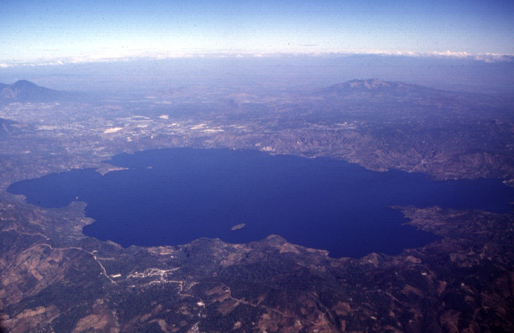 The 13 x 17 km Ilopango caldera is filled by one of El Salvador's largest lakes. The caldera, which has a scalloped 150-500 m high rim, lies immediately east of the capital city of San Salvador (upper left). The latest caldera collapse event occurred during the massive 536-550 CE eruption, which produced widespread pyroclastic flows and devastated early Mayan cities. Post-caldera eruptions formed a series of lava domes within the lake and near its shore. Photo by Carlos Pullinger, 1996 (Servicio Nacional de Estudios Territoriales, El Salvador).
