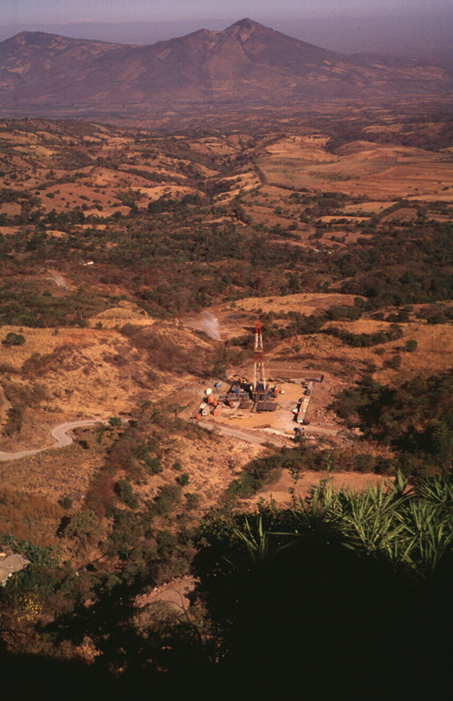 The Berlín geothermal area in the foreground is viewed from the SE on the flank of the Tecapa massif. The Pan-American highway traverses the base of the Tertiary volcanoes of Cerro Sihuatepeque (center) and Cerro Palacios (left) across the Río Lempa in the background. Photo by Carlos Pullinger, 1996 (Servicio Nacional de Estudios Territoriales, El Salvador).