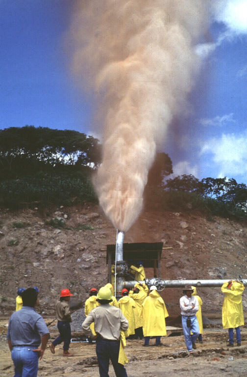 A plume rises from well CH-D during its opening in 1996. The Ahuachapán geothermal field was the first major field to be developed in El Salvador and has been operating since 1975. The geothermal field is located mostly in permeable, highly fractured Pliocene-Pleistocene volcanic rocks of the San Salvador formation that are capped by a series of young pyroclastic rocks and lava flows. A younger system of NW-trending faults localizes hydrothermal features within a series of step faults dropping to the north at the margin of the Central Salvadoran Graben. Photo by Carlos Pullinger, 1996 (Servicio Nacional de Estudios Territoriales, El Salvador).