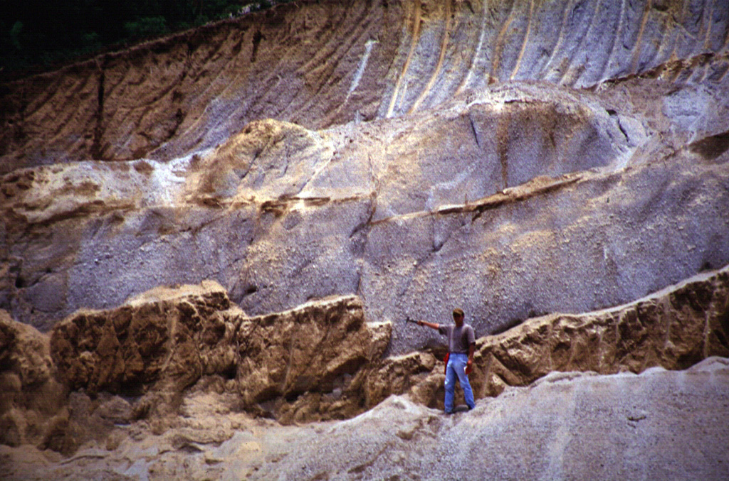 The thick light-colored unit the volcanologist is pointing to is the Arce fall deposit, overlying a paleosol and mafic ash and scoria deposits. This outcrop is about 15 km NW of the caldera rim. The biotite-rich rhyolitic Arce pumice-fall deposit was erupted from Coatepeque caldera about 72,000 years ago and was associated with formation of the SW part of the caldera. Deposits of the 84,000-year-old Los Chocoyos Ash from Atitlán caldera in Guatemala lie about 3 m below the base of the Arce deposit, but are not visible in this photo.  Photo courtesy of Carlos Pullinger, 1996 (Servicio Nacional de Estudios Territoriales, El Salvador).