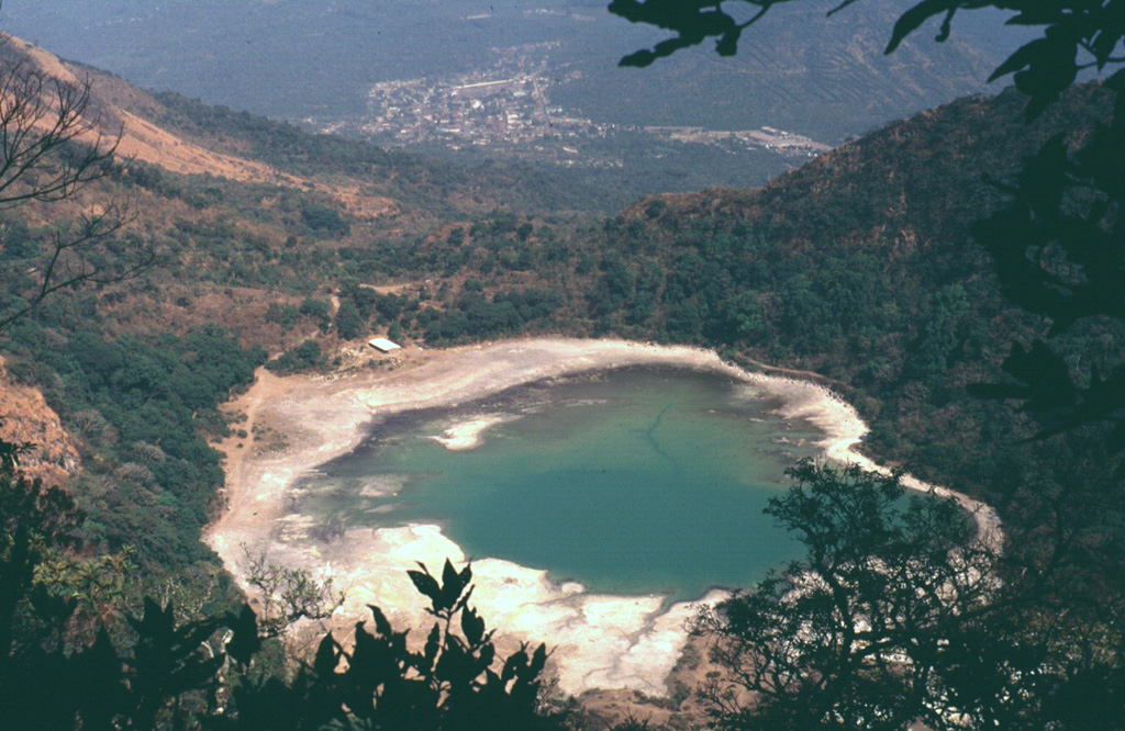 Laguna de Alegría is seen here from the summit of Tecapa volcano, looking SE with the town of Santiago de María in the background. The 600-m-wide crater lake lies about 300 m below the summit in this 1994 photo. Santiago de María is at the eastern end of the Tecapa volcanic complex, on the 900-m-high saddle between it and Cerro El Tigre volcano. Cerro Oromontique, on the flank of El Tigre volcano rise immediately to the right of the town. Photo by Carlos Pullinger, 1994 (Servicio Nacional de Estudios Territoriales, El Salvador).