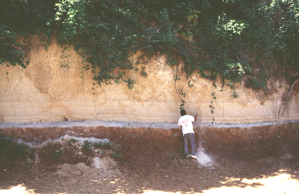 A volcanologist investigates an exposure of the Arce deposits on the eastern flank of Chilamatal caldera, about 10 km ENE of the rim of Coatepeque caldera. The Arce eruption around 72,000 years ago produced about 40 km3 of tephra and was associated with the first caldera-forming event at Coatepeque. The Arce deposits consist of two thick biotite-rich pumice fall deposits, separated by thin tephra deposits containing ash, pumice, and lithics. These ashfall deposits are distributed over much of western El Salvador. Photo by Carlos Pullinger, 1996 (Servicio Nacional de Estudios Territoriales, El Salvador).