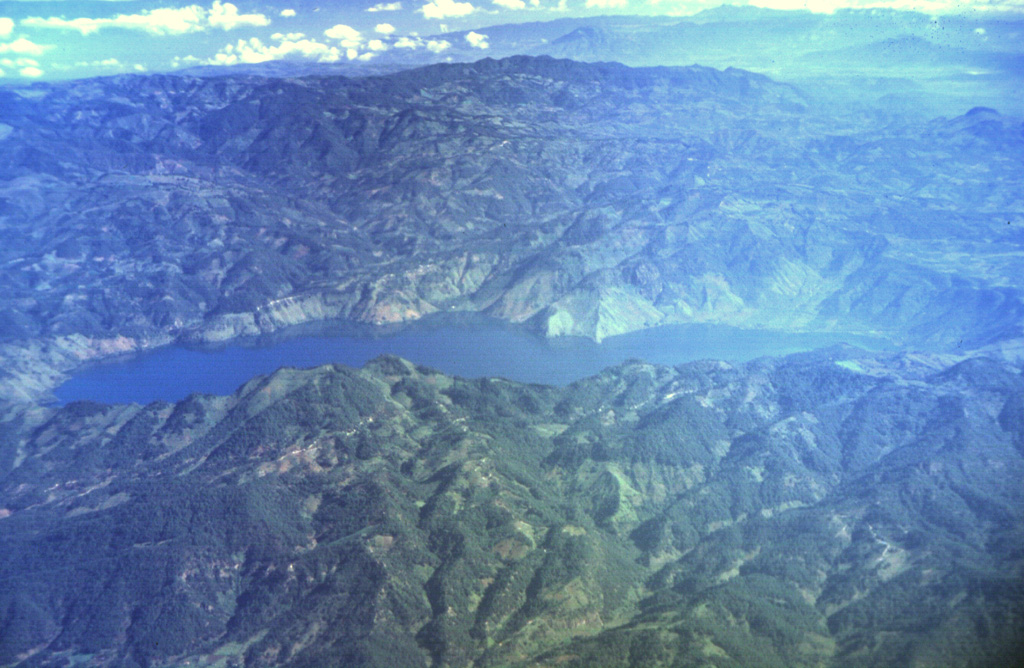 The figure-8-shaped Ayarza caldera appears elongated in this aerial oblique view from the SW.  The double caldera was formed during two major rhyolitic eruptions about 27,000 and 23,100 years ago.  These were among the youngest silicic eruptions in northern Central America.  The larger western caldera (left) has a maximum depth of 240 m, and the eastern caldera is 140 m deep.  Caldera walls rise an additional 300-600 m above the surface of Laguna de Ayarza. Photo by Carlos Pullinger, 1996 (Servicio Nacional de Estudios Territoriales, El Salvador).