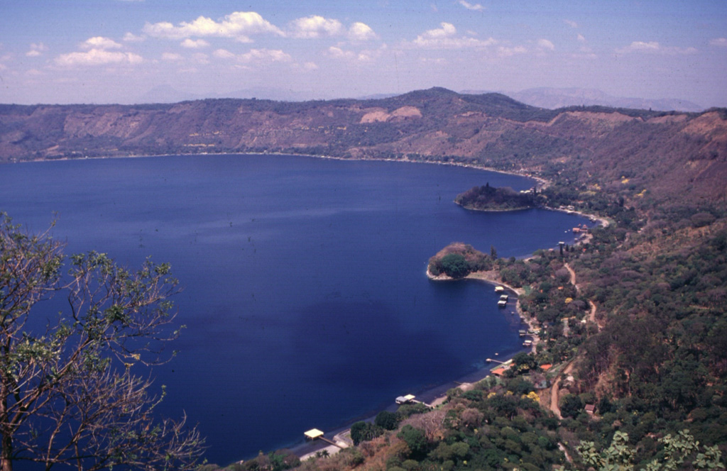 The Anteojos lava domes form peninsulas on the eastern shore of Lake Coatepeque, most of which lie beneath the lake surface. Four other domes formed in the opposite side of the caldera along a trend that passes through Izalco volcano to the SW. Two scoria cones on the horizon erupted along caldera ring faults. Photo by Carlos Pullinger, 1996 (Servicio Nacional de Estudios Territoriales, El Salvador).
