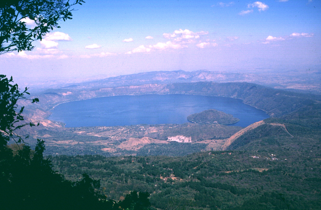 Coatepeque caldera is seen here from the summit of Cerro Verde to the SSW, a flank cone of Santa Ana volcano. Lago de Coatepeque fills the NE part of the 7 x 10 km caldera. The younger SW side of the caldera extends into Santa Ana volcano and to the sudden break in slope seen in the lower right of the photo. The caldera floor is higher on this side as a result of the accumulation of volcaniclastic debris from Santa Ana and the eruption of a series of post-caldera lava domes, one of which forms the island in the lake. Photo by Carlos Pullinger, 1996 (Servicio Nacional de Estudios Territoriales, El Salvador).