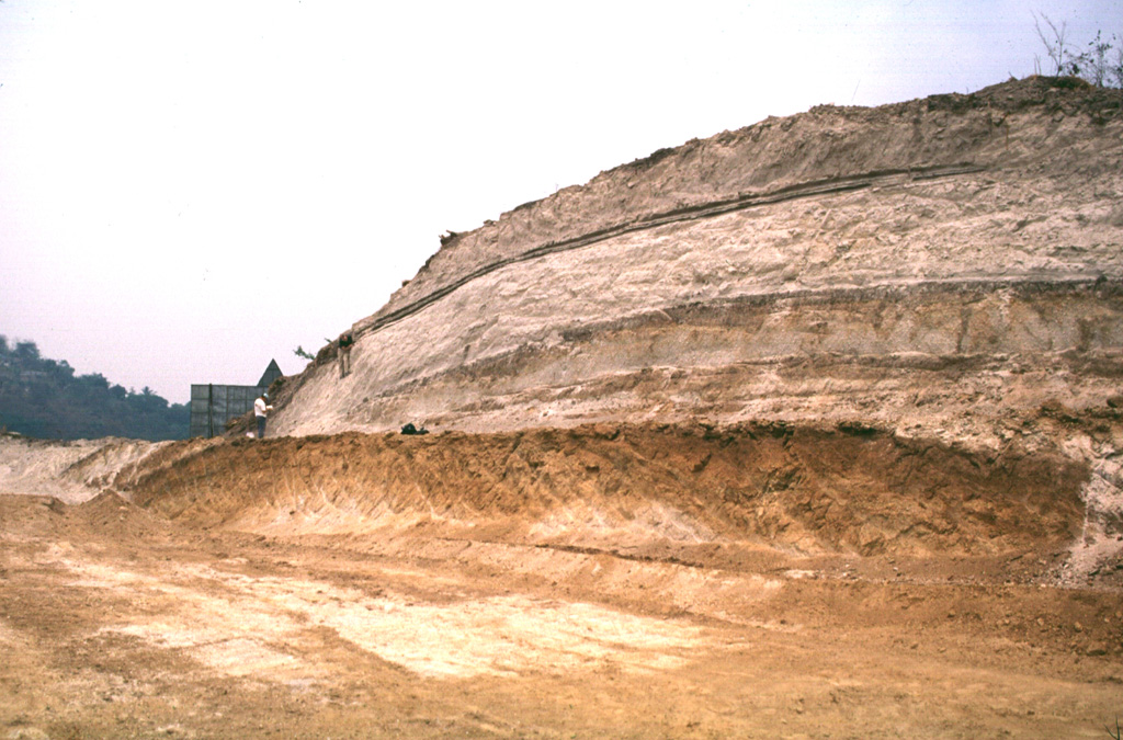 Four major pyroclastic units associated with the incremental formation of Ilopango caldera are exposed in this quarry. The Tierra Blanca (White Soil) unit that was emplaced over much of central and western El Salvador consists of (from bottom to top) the Pleistocene TB4 (the orange-colored unit at the base), TB3, and TB2 units (separated by thin soils), and the Holocene TBJ unit. The latter is called the Tierra Blanca Joven (the young Tierra Blanca) and was erupted about 1,500 years ago. Note the geologist on the left side of the outcrop for scale.    Photo by Carlos Pullinger, 1996 (Servicio Nacional de Estudios Territoriales, El Salvador).