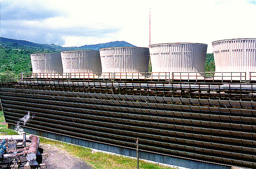 The cooling towers of the Ahuachapán-3 power plant are part of a geothermal field that has been producing for more than a quarter century.  The liquid-dominated geothermal reservoir has a base temperature of about 240 degrees centigrade.  It is located on the northern flank of the Apaneca (Cuyanausul) Range along the southern margin of the Salvadoran central graben.  Consequently it is lower to the north and NW, where it has been affected by graben subsidence. Photo courtesy of Comisión Ejecutiva Hidroeléctricia del Río Lempa (CEL).