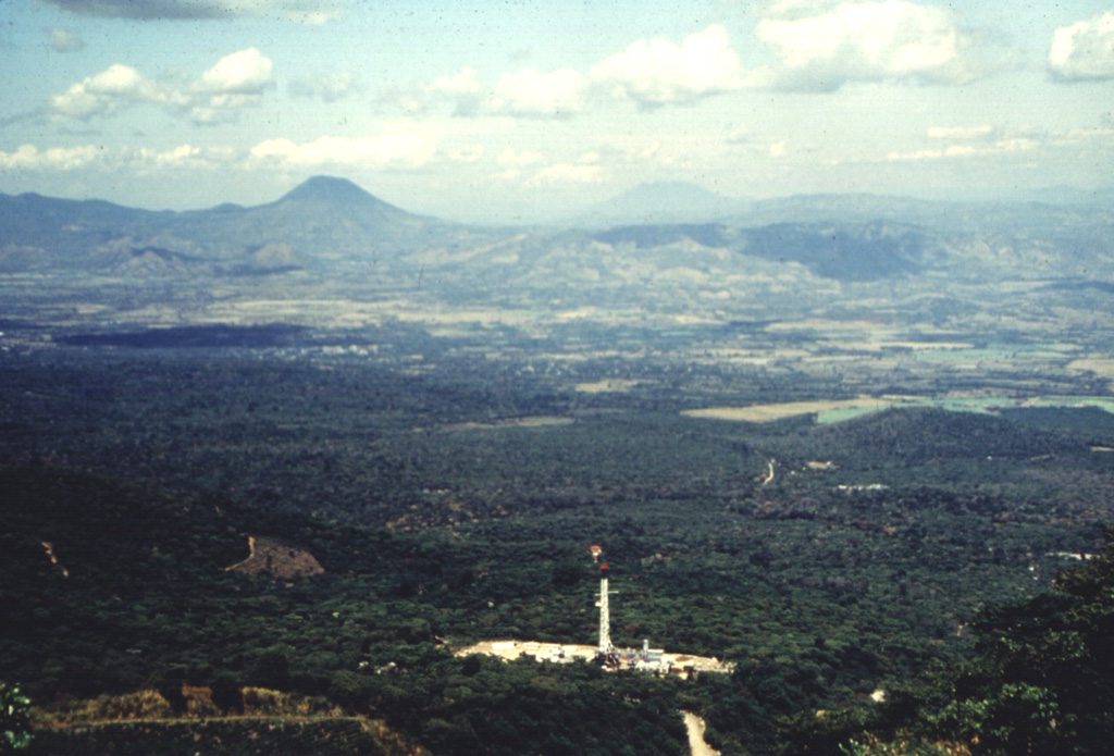This view from the Apaneca Range shows the CH-A well and drill rig of the Ahuachapán geothermal field in the foreground. The peak on the left horizon across the lowlands of El Salvador's interior valley is Volcán Chingo, along the El Salvador/Guatemala border. The flatter peak to the far right is Volcán Suchitán in Guatemala. Photo by Comisión Ejecutiva Hidroeléctricia del Río Lempa (CEL), 1992.