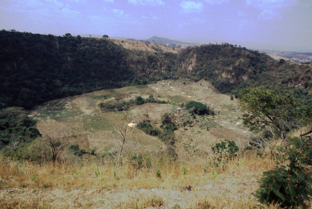 Hoyo de Caldera is a maar crater located NW of Laguna de Apastepeque. The crater is 700 m wide and 140 m deep, seen here from the SE in 1999.   Photo by Giuseppina Kysar, 1999 (Smithsonian Institution).