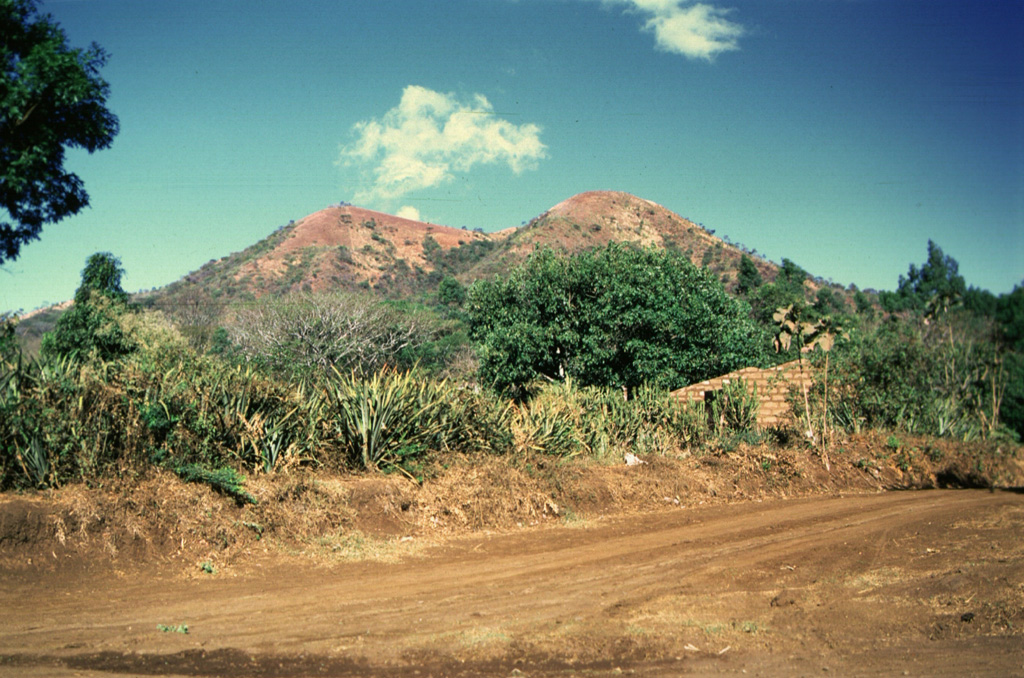 Loma Los Siete Cerros (Peak of the Seven Hills) is part of the Volcán Chingo volcanic field. This complex of overlapping scoria cones on the Salvadoran side is seen here from the east and is one of many flank vents. Among the youngest vents are those that produced lava flows on the NW side  in Guatemala. Other young flows erupted from an intermittent chain of cones extending N-S on both side of the summit. Photo by Giuseppina Kysar, 1999 (Smithsonian Institution).