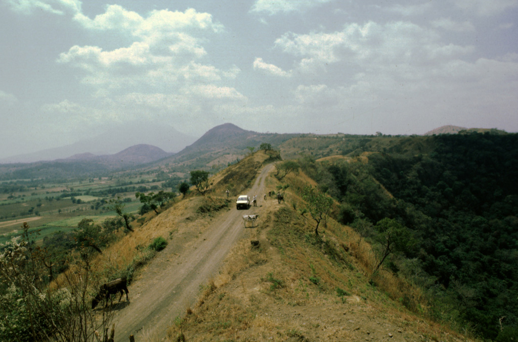 Several different features of the Apastepeque volcanic field can be seen in this view from the Hoyo de Calderas crater rim. Two lava domes are seen in the distance to the left, Cerro Las Delicias and Cerro Santa Rita (far left). The larger volcano in the haze behind Cerro Santa Rita is San Vincente. Photo by Giuseppina Kysar, 1999 (Smithsonian Institution).