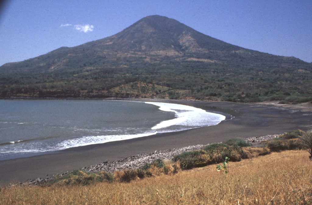 Conchagua volcano towers above sandy beaches along the Gulf of Fonseca at the SE tip of El Salvador.  The 1225-m-high stratovolcano has a conical profile, but has been extensively eroded.  The easternmost of two major summits, Cerro de la Bandera, is seen in this view from Punta el Chiquirín and appears to be younger in age.  Recently active fumarolic areas form barren spots on both peaks of this little-studied volcano.  Historical reports of eruptions appear to be erroneous, and may refer to landslides associated with earthquakes. Photo by Rick Wunderman, 1999 (Smithsonian Institution).