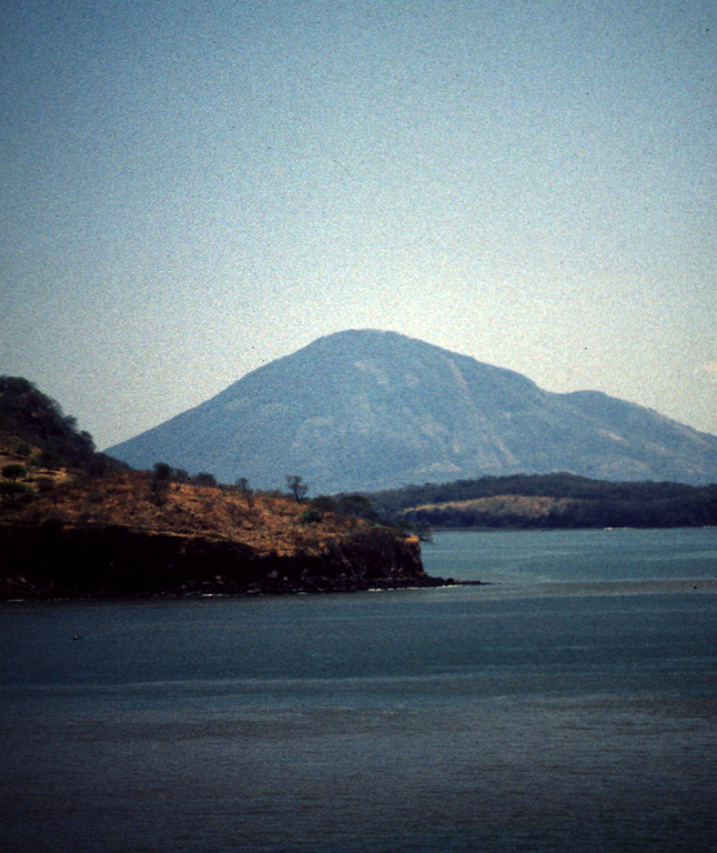 Isla el Tigre in Honduras is seen here across the Gulf of Fonseca from Punta el Chiquirín on the eastern tip of El Salvador.  The morphologically youthful volcano rises 783 m above the gulf and is the southernmost in Honduras.  A valley on the SW flank (right) extends to the sea and disrupts the symmetry of the volcano. Photo by Rick Wunderman, 1999 (Smithsonian Institution).