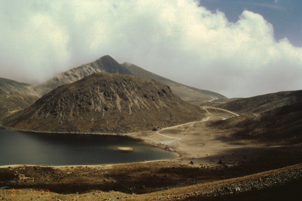 The rounded El Ombligo dome is one of the youngest features in the summit crater of Nevado de Toluca. The dome separates the crater floor into two lakes, the largest of which on the SW side of the crater (left) is called Lake of the Sun. The other lake, known as the Lake of the Moon, lies beyond the right side of the dome in this view, which shows the road leading into the summit crater to the right.  Photo by José Macías, 1995 (Universidad Nacional Autónoma de México).